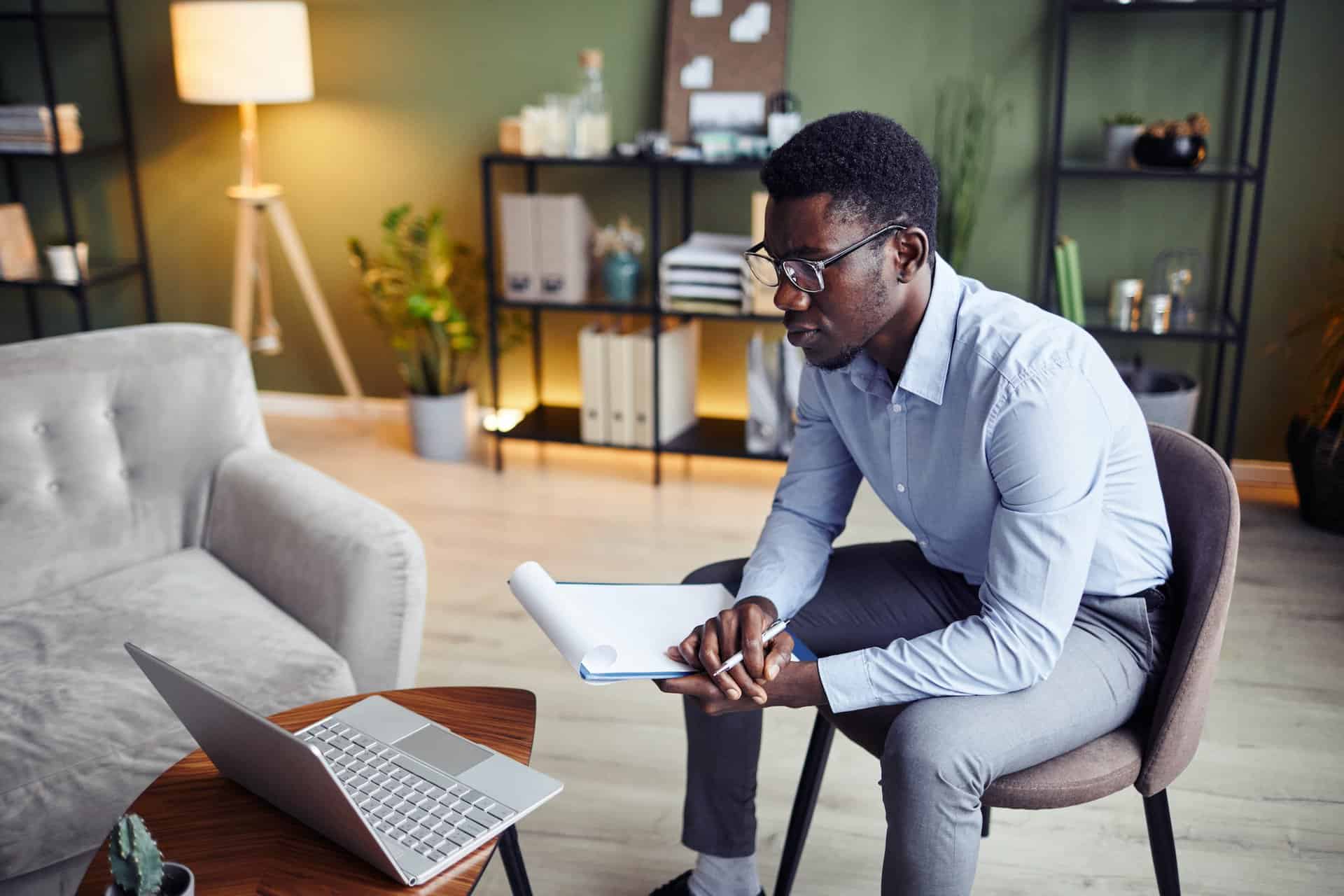 Modern professional man working at home office with laptop, notepad, and coffee, focusing on business tasks.